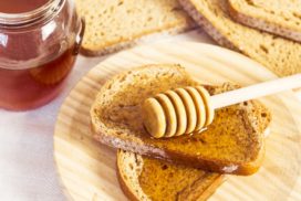 jak spożywać miód, zdrowotne właściwości miodu - zdjęcie kromek chleba posmarowanego miodem, na jednej z nich leży nabierak do miodu, obok słoiczek z miodem
